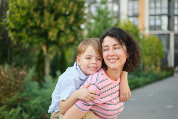 Fototapeta na wymiar young mother and son smiling looking at the camera in modern residential complex. Having fun together, happy parenting, new home concept. Bright summer day in the urban background. High quality photo