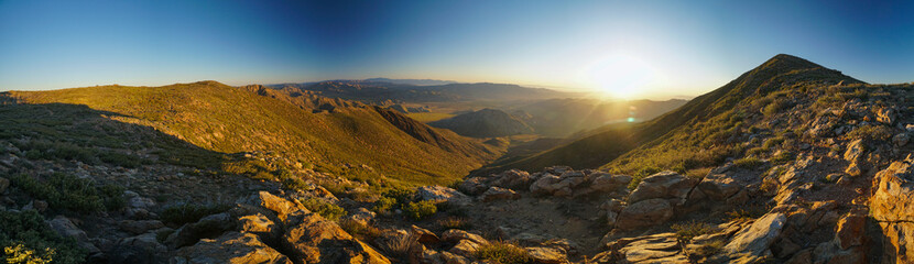 A panoramic view of a mountain range with a sun setting in the background