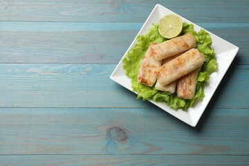 Delicious fried spring rolls on light blue wooden table, top view. Space for text