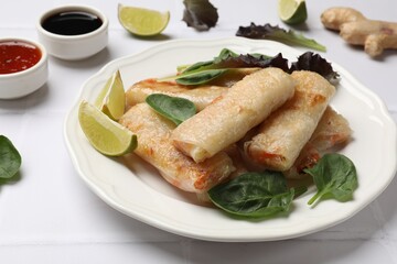 Plate with tasty fried spring rolls and spinach on white tiled table, closeup