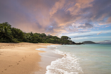 Deserted wide sandy beach with turquoise blue sea. Tropical plants of a bay at sunset in the...