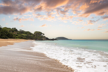 Fototapeta na wymiar Deserted wide sandy beach with turquoise blue sea. Tropical plants of a bay at sunset in the Caribbean. Plage de Cluny, Basse Terre, Guadeloupe, French Antilles,