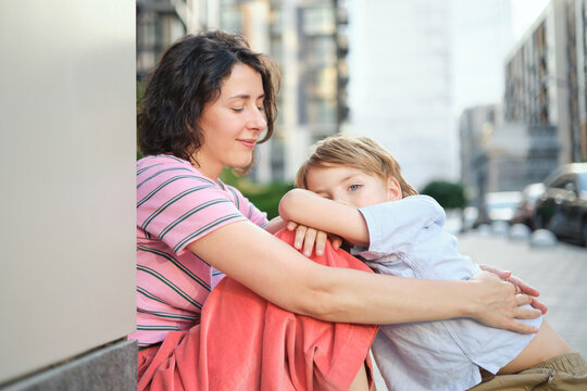 Adorable mother and son smiling happy having fun at city background. Motherhood concept, hugging. Boy 8 years old with mother in bright clothes enjoying summer day. High quality photo