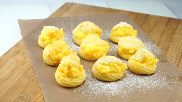 Profiteroles or cream puff with filling, falling powder sugar topping. Fresh homemade Cream Puffs, cake, tasty French choux puff, ecler, dessert closeup. Pastries