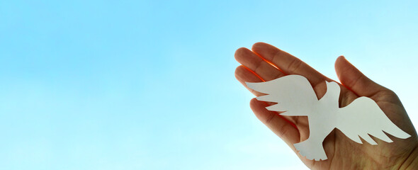 White paper origami bird on blue sky background. World Day of Peace. Day Against Humiliation....