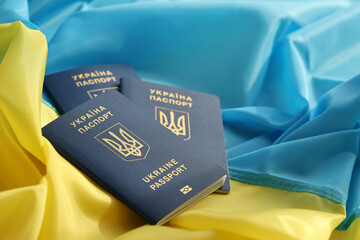 Three Ukrainian biometrical passports on folded waving flag of Ukraine country close up