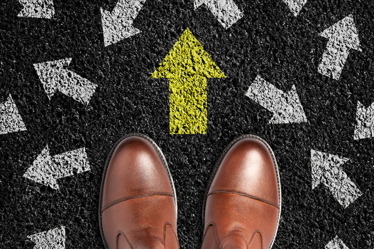 Men boots on an asphalt road. Yellow arrows pointing in different directions. Top view. The concept of choosing the right path. Business. Lifestyle.