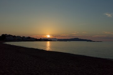 Sun going down late in the evening at Sunset beach in clear spring weather, Agioi Apostoloi, Crete, Greece.
