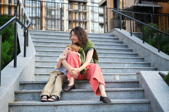 Happy family: mother and child son hugging and laugh sitting on the city stairs. motherhood concept, togetherness, love emotion. Urban city concept, residential complex in Ukraine. High quality photo