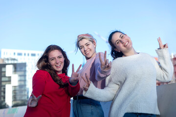 Three happy friends posing with peace signs