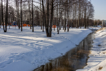 Thaw in the city park, snow melting, accumulated water in the ditch. spring flood, sunny day in the...