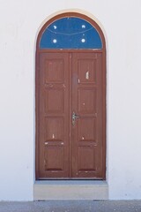 Old brown wooden door with glass arch on a white stone building.