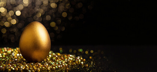 Golden easter egg on pearls and glitter sparkling surface. Black background with bokeh effect: deluxe digital image with space for text.
