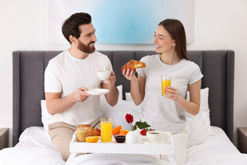 Happy couple having breakfast and talking on bed at home