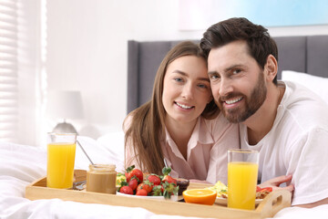 Family portrait of happy couple with tray of tasty breakfast on bed at home. Space for text