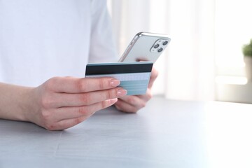 Online payment. Woman with smartphone and credit card at white table, closeup