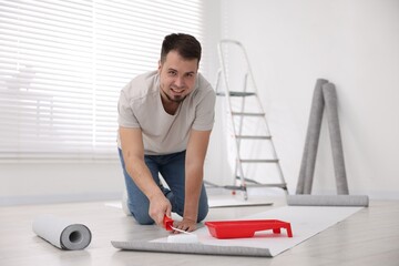 Man applying glue onto wallpaper sheet in room