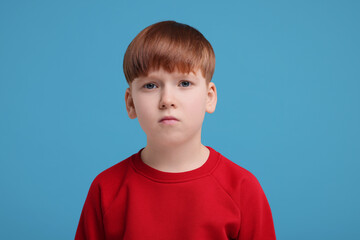 Portrait of sad little boy on light blue background