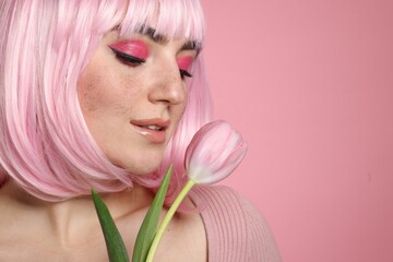 Beautiful woman with bright makeup, fake freckles and tulip on pink background, closeup. Space for text