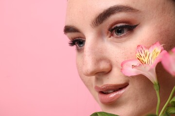 Fototapeta premium Beautiful woman with fake freckles and flowers on pink background, closeup. Space for text