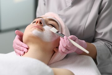 Cosmetologist applying mask on woman's face, closeup