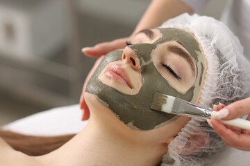 Cosmetologist applying mask on woman's face in clinic, closeup