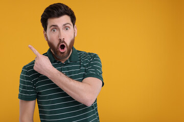 Surprised man pointing at something on yellow background, space for text