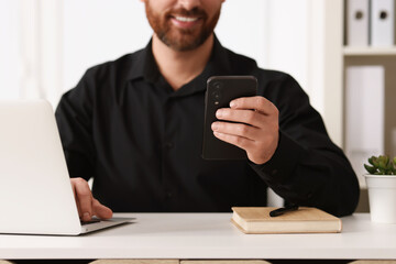 Smiling man using smartphone at table in office, closeup