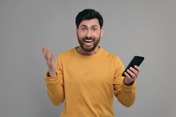 Emotional man with smartphone on grey background