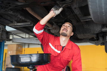 Male mechanic working at garage. Professional Asian male mechanics checks, repair and maintenance underneath lifted car at auto car repair service. Car service and Maintenance concept