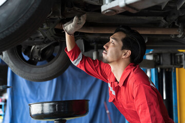 Male mechanic working at garage. Professional Asian male mechanics checks, repair and maintenance underneath lifted car at auto car repair service. Car service and Maintenance concept