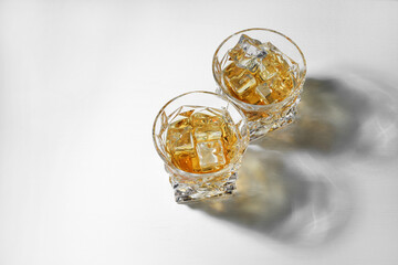Whiskey with ice cubes in glasses on white table, above view. Space for text