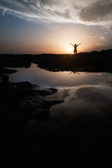 woman on sea shore at sunset raising arms