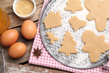 Ingredients and raw Christmas cookies in different shapes on wooden table, flat lay