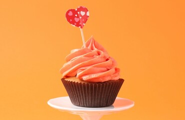 Delicious cupcake with bright cream and heart topper on orange background