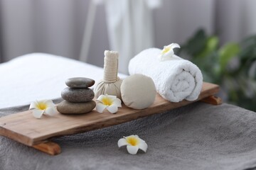Fototapeta na wymiar Stacked spa stones, flowers, herbal bags and towel on massage table indoors