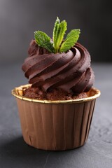 Delicious chocolate cupcake with mint on black textured table, closeup