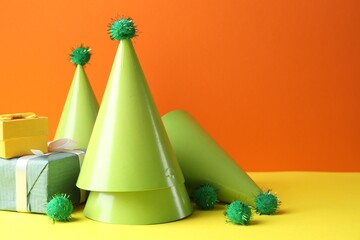 Party hats and gift boxes on yellow table against orange background, space for text