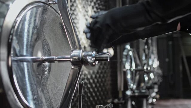 Hands of a worker in black rubber gloves rotate the tank hatch valve at a winery.