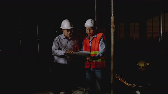 Working Late at Night in construction site. Engineers and architects in safety uniforms and hard hats talk and review blueprints as they stand in a building site. worker