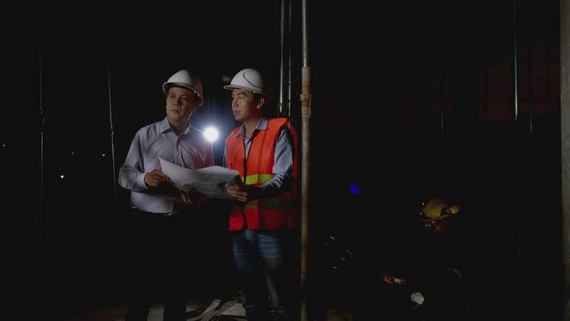 Working Late at Night in construction site. Engineers and architects in safety uniforms and hard hats talk and review blueprints as they stand in a building site. worker