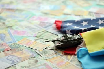 Fototapeta na wymiar Toy tank on US flag and ukrainian flag on many banknotes of different currency. Background of war funding and military support between United States and Ukraine