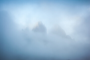 The sharp peaks of Tre Cime di Lavaredo are visible through the mist. Sexten Dolomiti, South Tyrol, Europe. - obrazy, fototapety, plakaty