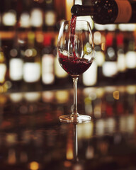 Botella de vino llenando una copa, posada sobre un mostrados, sobre fondo desenfocado de un grupo de. botellas expuestas en una vitrina - obrazy, fototapety, plakaty