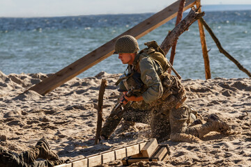 Historical reconstruction. An American infantry soldier from the World War II  fighting on the beach. - obrazy, fototapety, plakaty