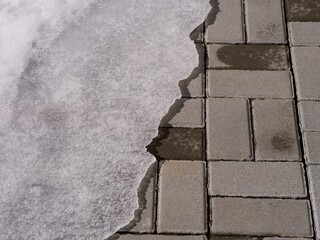 A large piece of ice on stone tiles. Spring time