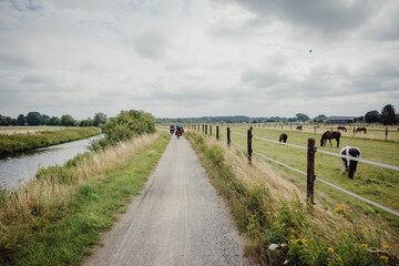 Familie radelt während einer Radreise auf einem idyllischen Radweg zwischen einem Fluss und einer Pferdewiese durch das westliche Münsterland