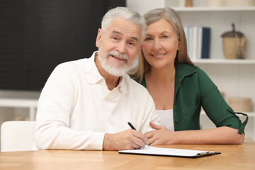Happy senior couple signing Last Will and Testament indoors