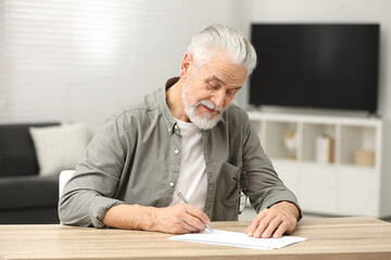Senior man signing Last Will and Testament at table indoors