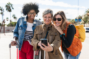 Three women tourist friends using cell phone, traveling enjoying weekend vacation - obrazy, fototapety, plakaty